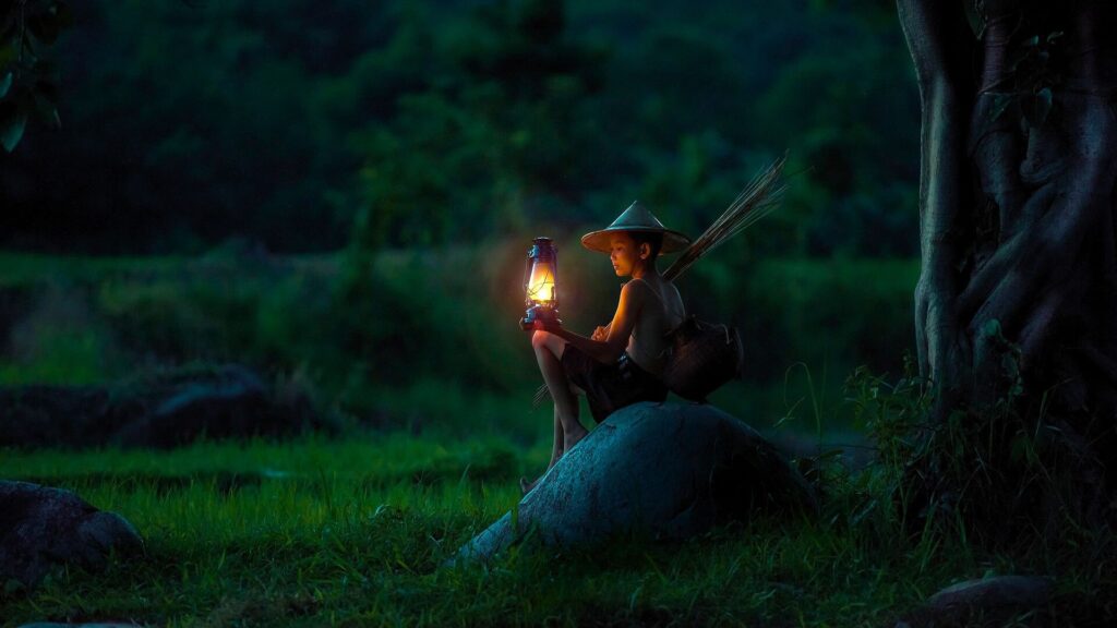 a village boy sitting on a rock in a forest with a burning lantern in hand